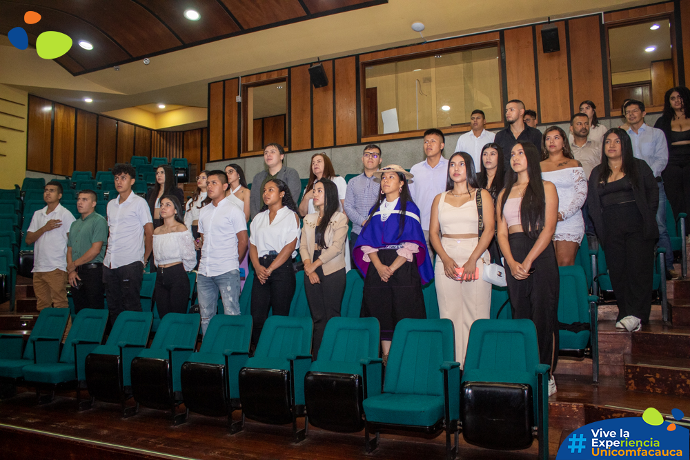Fotografía grupal de estudiantes de pie de Unicomfacauca y la Universidad Cooperativa de Colombia entonando el himno nacional.