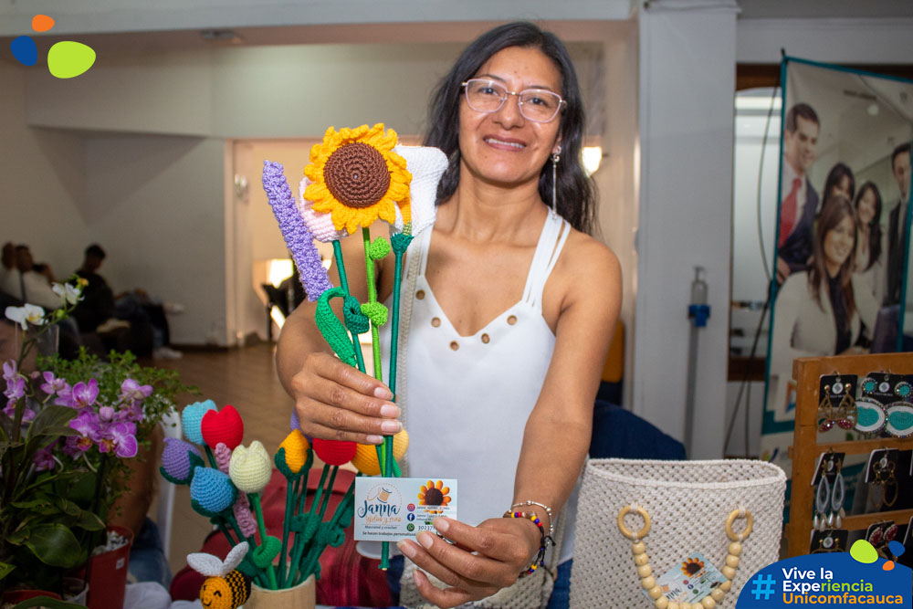 Emprendedora mostrando unas flores en crochet a la cámara mientras sostiene su tarjeta de presentación.