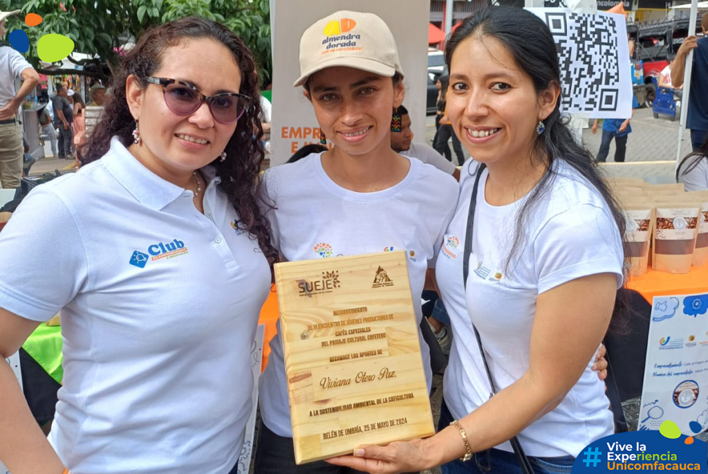 Viviana Otero Díaz siendo reconocida por su esfuerzo, dedicación, compromiso y contribución a la sostenibilidad ambiental en la caficultura colombiana. Al lado de ella se encuentra la Coordinadora de la Unidad de Emprendimiento, Magaly Cerón, y la asistente de Proyección Social, Katherine Cortés.